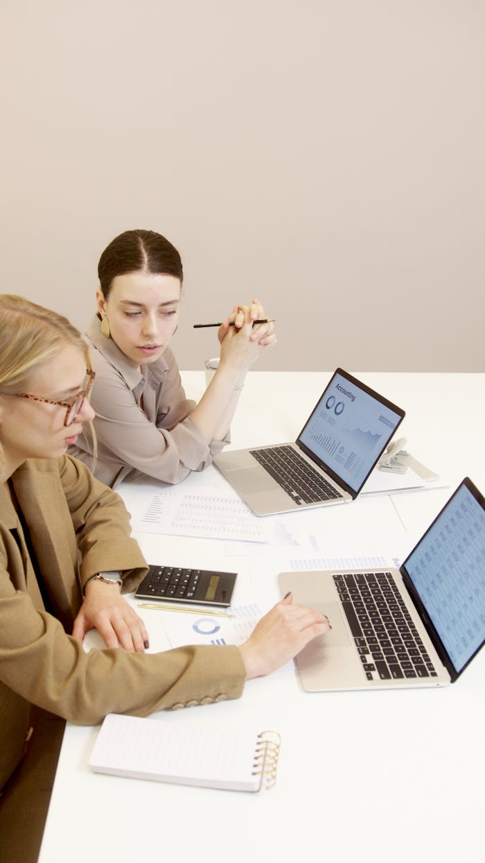 The Art of Drawing Readers In: Your attractive post title goes here Two businesswomen using laptops to analyze financial documents in an office setting.